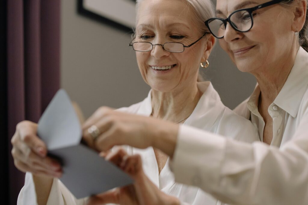 Two older women, dressed in white shirts and wearing glasses, share a moment of connection as they read a greeting card together. The card evokes the essence of personalized content, fostering a sense of closeness and shared experience.